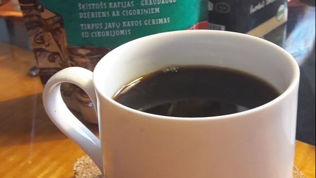 Kahvikuppi, jossa mustaa juomaa, taustalla sikurikahvipussi.